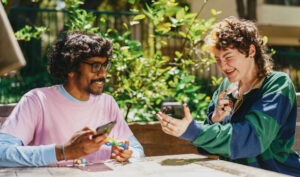 two people sitting at a table outside with their phones